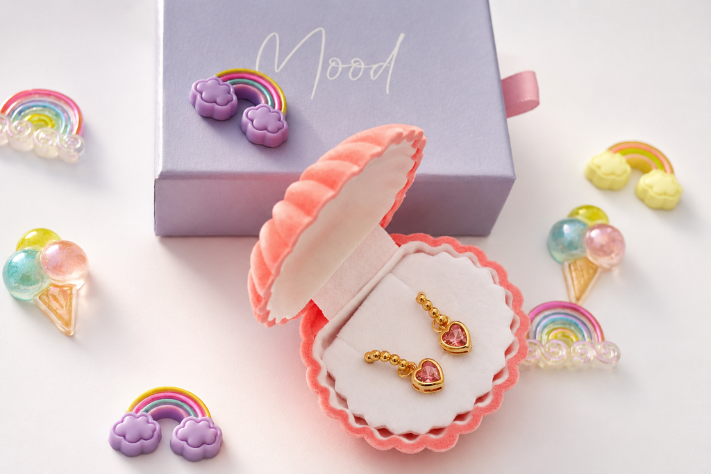 Gold heart-shaped earrings with pink heart inlays, displayed in an open pink clamshell jewelry box next to a lavender box labeled 'Mood'.