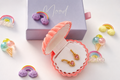 Gold heart-shaped earrings with pink heart inlays, displayed in an open pink clamshell jewelry box next to a lavender box labeled 'Mood'.