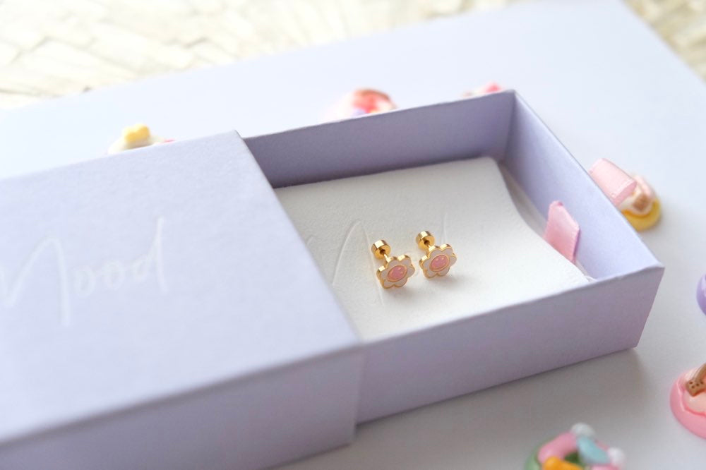 Pair of gold and pink earrings in a white jewelry box on a light surface.