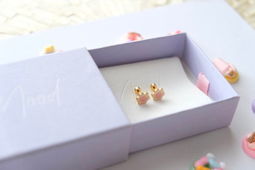 Pair of gold and pink earrings in a white jewelry box on a light surface.