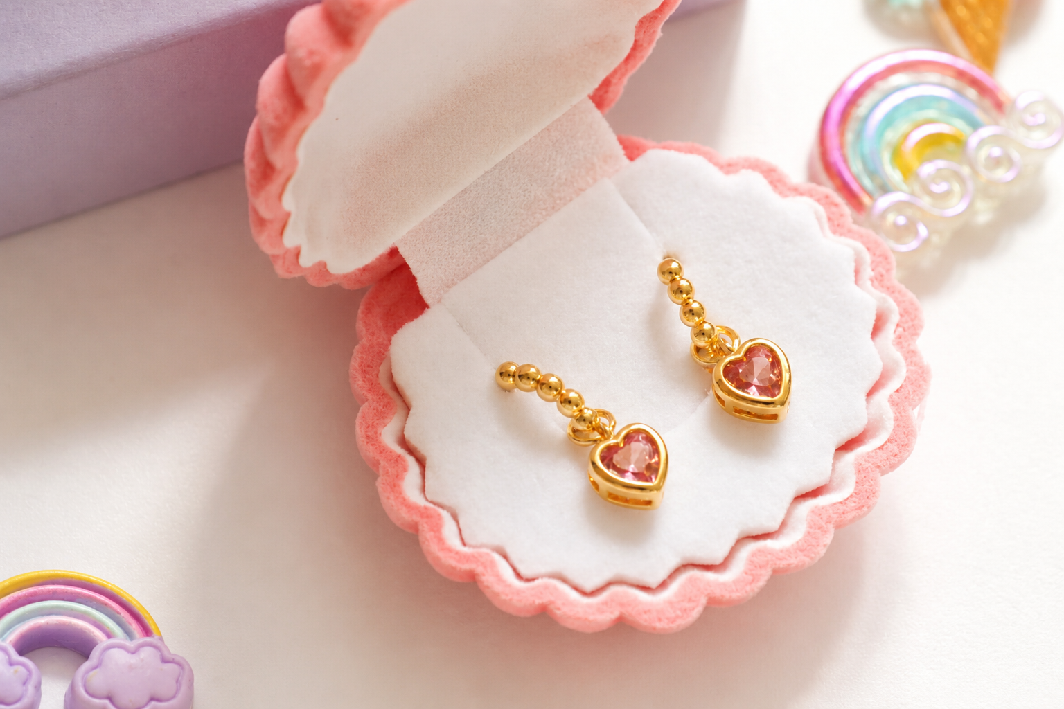 Gold heart-shaped dangle earrings with pink heart charms, displayed in a pink scalloped jewelry box on a white surface.