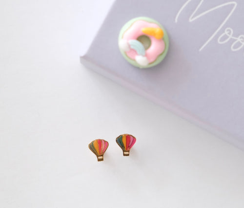Colorful donut and hot air balloon earrings on a white surface with a blurred background.
