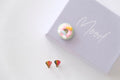 Colorful donut-shaped earrings on a white surface with a notebook in the background.