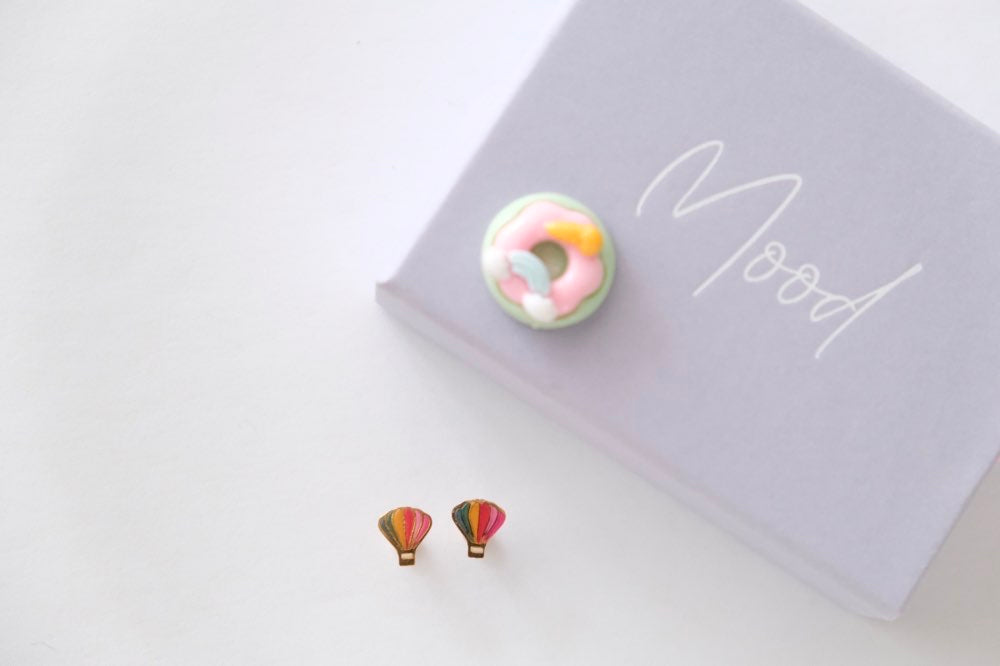 Colorful donut-shaped earrings on a white surface with a notebook in the background.