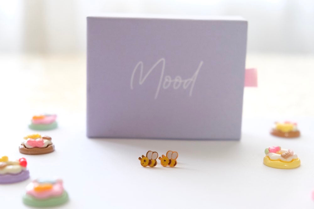 Bee-shaped earrings in front of a 'Mood' branded box on a white background