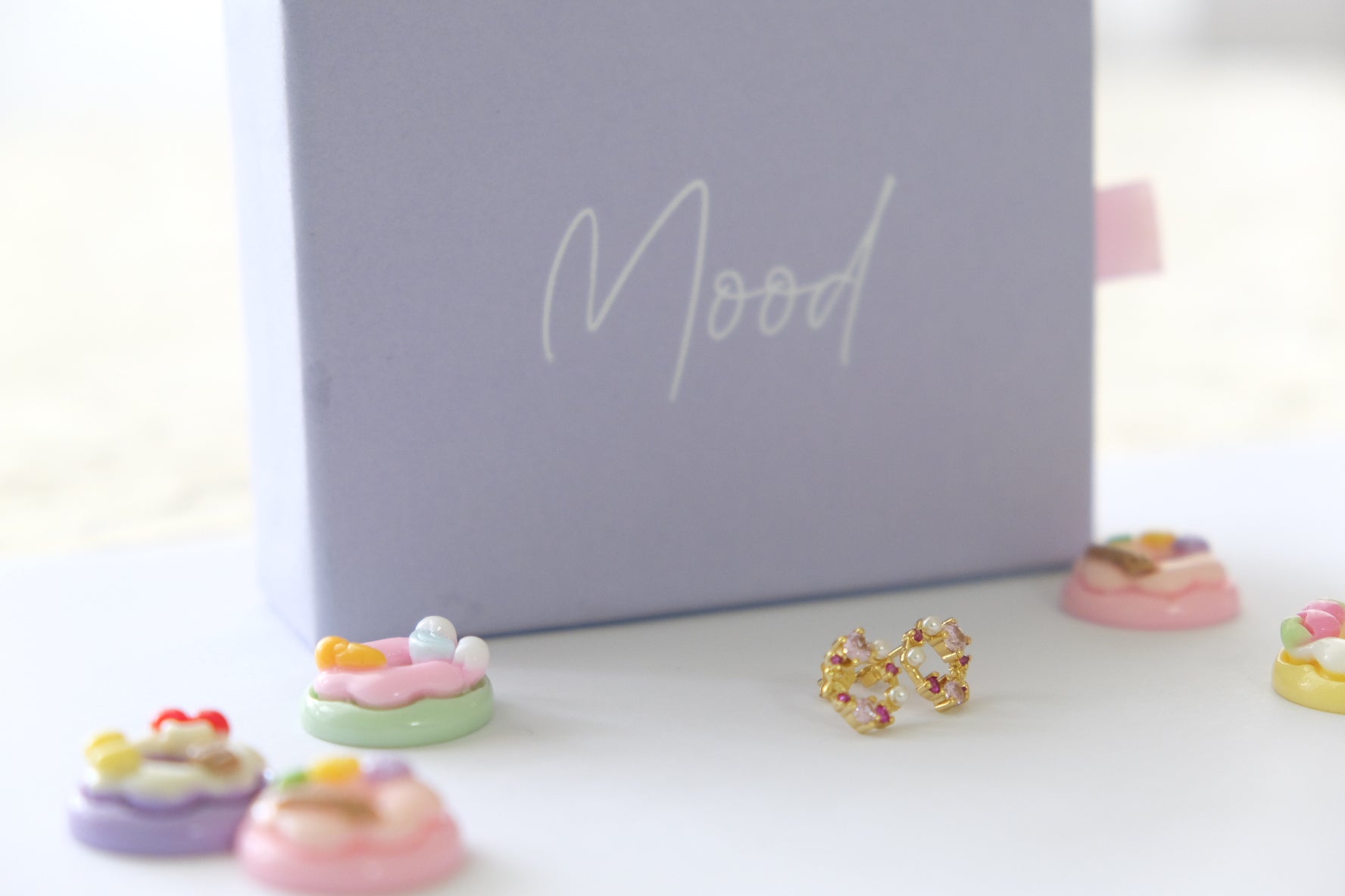 Colorful donut-shaped earrings in front of a 'Mood' branded box.