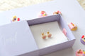 Pair of gold earrings with pink heart designs in a white box on a light surface.