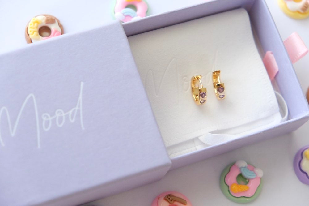 Gold earrings in a 'Mood' branded box with colorful donut-shaped objects around.