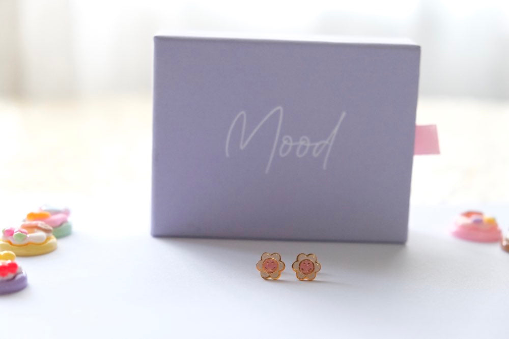 Floral earrings on a white surface with a 'Mood' branded box in the background.