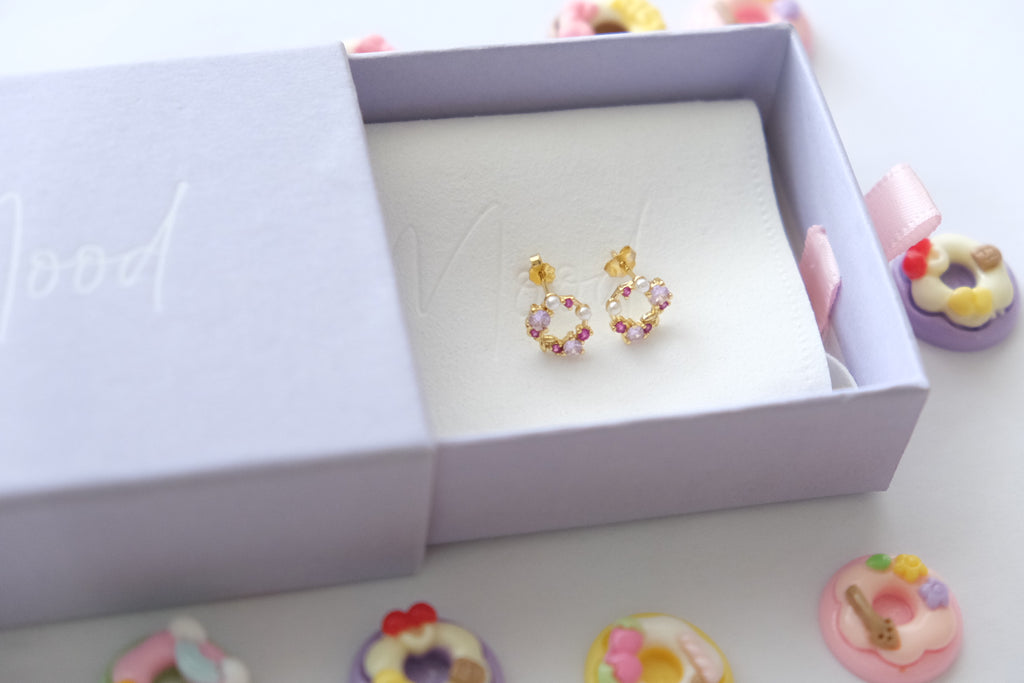 Colorful hoop earrings in a white box with decorative donut candies around.