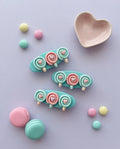 Pastel-colored hair clips with heart and flower designs on a light purple background.