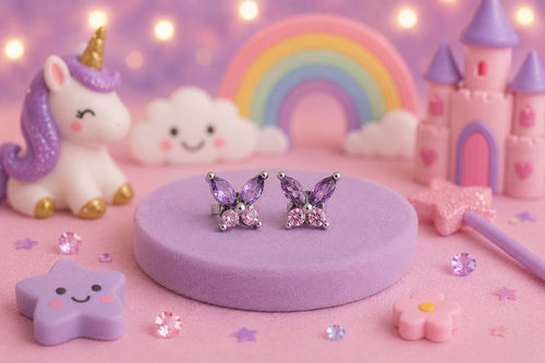 A pair of butterfly-shaped stud earrings with purple crystals and silver settings, displayed on a round purple pedestal. The background is a whimsical, pastel-themed scene featuring a unicorn, castle, rainbow, and stars.