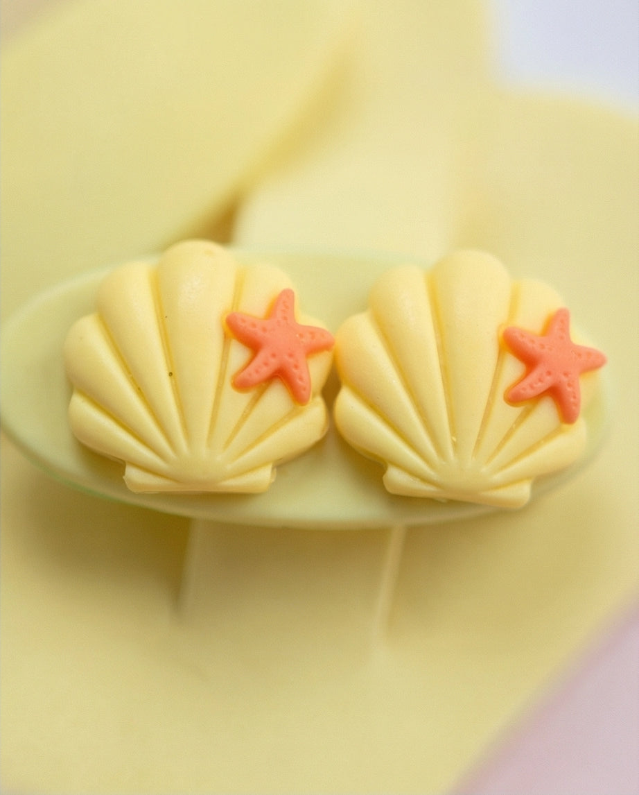 Two shell-shaped cookies with red starfish on a yellow plate